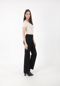 Jeans negros de cintura alta combinados con una blusa ajustada crema, que presenta un escote cuadrado, una textura suave y botas negras de tacón.