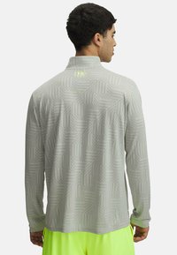 Szary longsleeve z geometrycznym wzorem, z kołnierzykiem stojącym oraz subtelnym logo w neonowym żółtym kolorze z tyłu.