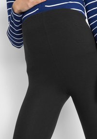 Leggings noirs en tissu extensible avec une texture lisse et une taille élastique, dotés de poches latérales pour le rangement.