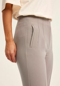 Harmaat räätälöidyt housut, joissa on sileä pinta, kapea istuvuus ja sivutaskut. Kankaassa on hieno pystysuora raitakuosi lisäämään yksityiskohtia.