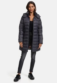 Puffjacka i mörkgrå, med dragkedja fram, huva och quiltad design. Pairad med svarta jeans och svarta sneakers.