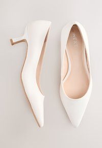 Hvide spidse hæle med en glat tekstur, der har en slank, lysebrun stilet-hæl og et diskret mærkelogo indvendigt.