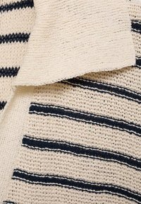 Tissu en tricot crème avec des rayures horizontales bleu marine, montrant la texture et le superposition de deux pièces textiles qui se chevauchent.