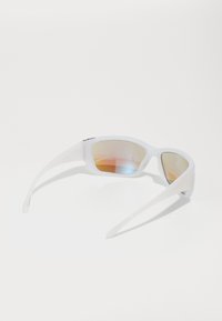 Lunettes de soleil avec une monture en plastique blanc, de forme courbée, verres miroir affichant un dégradé de rose à orange, et branches fines.