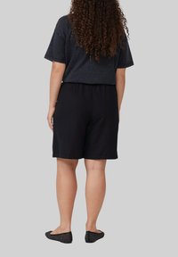 Zwarte katoenen shorts met een elastische tailleband, gecombineerd met een donkergrijze T-shirt met korte mouwen. Zwarte instap schoenen met een geperforeerd ontwerp.