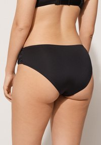 Černé vysoké bikinové kalhotky, hladký materiál, detail s řasením po stranách, střední výška, minimální pokrytí, bezšvový design.