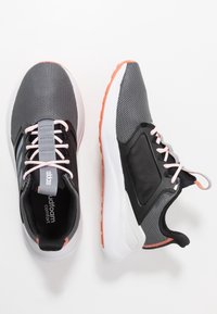 Un par de zapatillas de running Adidas en gris y negro con mediasoles blancos y acentos en coral, que presentan tejido de malla y cordones rosas sobre un fondo blanco.