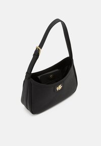 Czarna torba na ramię wykonana z gładkiego materiału z złotym logo jako akcentem. Posiada pojedynczy pasek i zaokrąglony kształt z zapięciem na zatrzask.