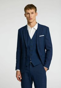 Mornarsko modra trodelna obleka z teksturiranim zaključkom, ki vključuje enoredni suknjič, brezrokavnik s petimi gumbi in belo srajco.