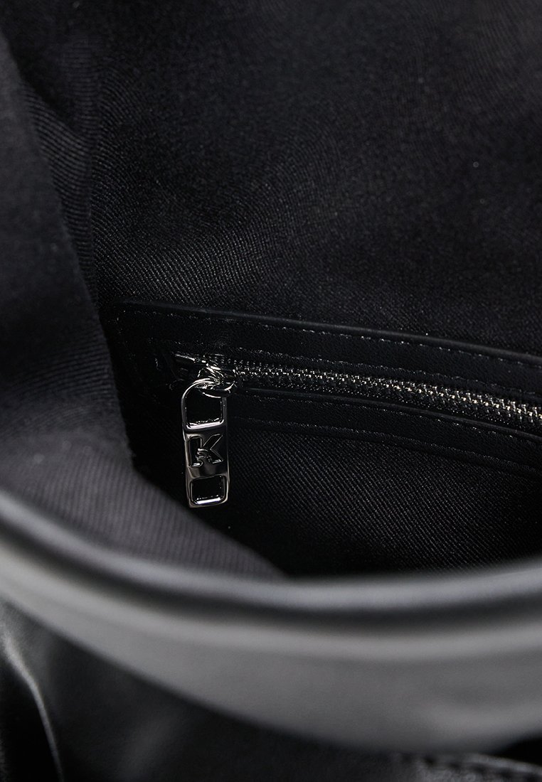 Interior negro de un bolso, con un bolsillo con cremallera y un tirador plateado. La tela tiene un acabado suave y texturizado.