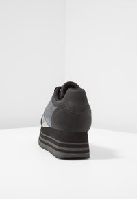 Musta urheilukenkä, jossa on tekstuuripinta, harmaat yksityiskohdat ja paksu musta-harmaa raidoitettu pohja; sisältää pehmustetun kantapään mukavuutta varten.