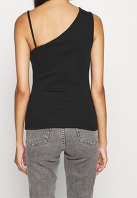 Black ribbed tank top with a single shoulder strap and an asymmetrical neckline, paired with gray high-waisted jeans featuring back pockets.