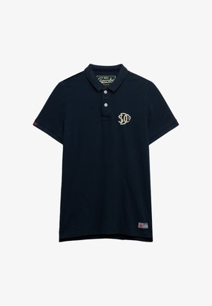 Polo blu navy scuro in cotone. Presenta un colletto, tre bottoni e un logo color crema sul petto. Maniche corte e orlo dritto.