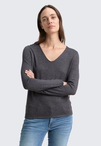 Szürke hosszú ujjú póló V-nyakú kialakítással, puha anyagból készült, laza szabású és minimalista stílusú. Világoskék farmerral párosítva.