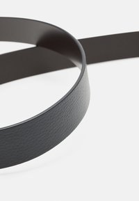 Cintura in pelle grigio scuro con una finitura testurizzata, caratterizzata da un design elegante e arrotondato. La parte posteriore ha un aspetto liscio e opaco.