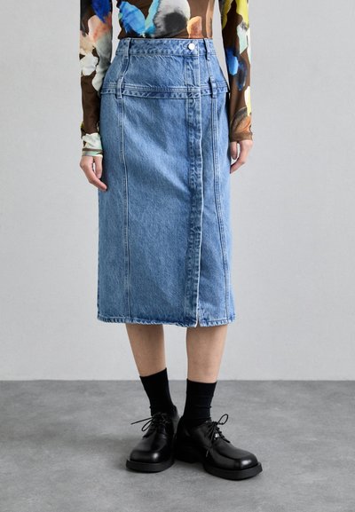 Denim midi-skjørt med frontknapp, kontrasterende sømmer og sidelommer. Kombinert med svarte snøresko og mørke sokker.