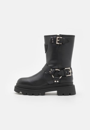 Fekete bőr bokacsizma masszív talppal, több csattal és kör alakú díszítéssel. Simás textúrával és matt felülettel.