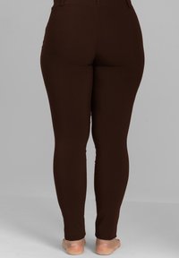 Braune Leggings mit glatter Textur, figurbetontem Design und ohne sichtbare Hardware. Der Stoff wirkt dehnbar und bequem.
