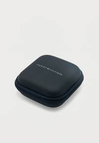 Μικρή μαύρη τετράγωνη θήκη με φερμουάρ, στρογγυλεμένες άκρες και το λογότυπο Tommy Hilfiger στην κορυφή, σε λευκό φόντο.