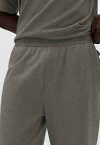 Šedé teplákové kalhoty s elastickým pasem s nápisem "PULL&BEAR". Hladká tkanina, volný střih a detail boční kapsy.