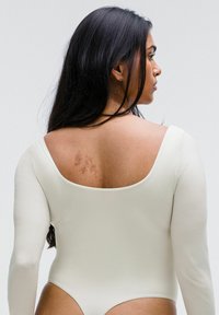 Bodysuit blanco de manga larga con un escote profundo en la espalda y un diseño ajustado, que resalta una tela suave y un ligero brillo.