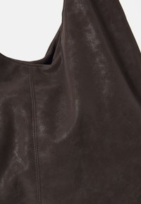 Sac en cuir brun foncé avec une texture lisse et un éclat subtil. Présente une silhouette courbée et des détails de couture visibles.