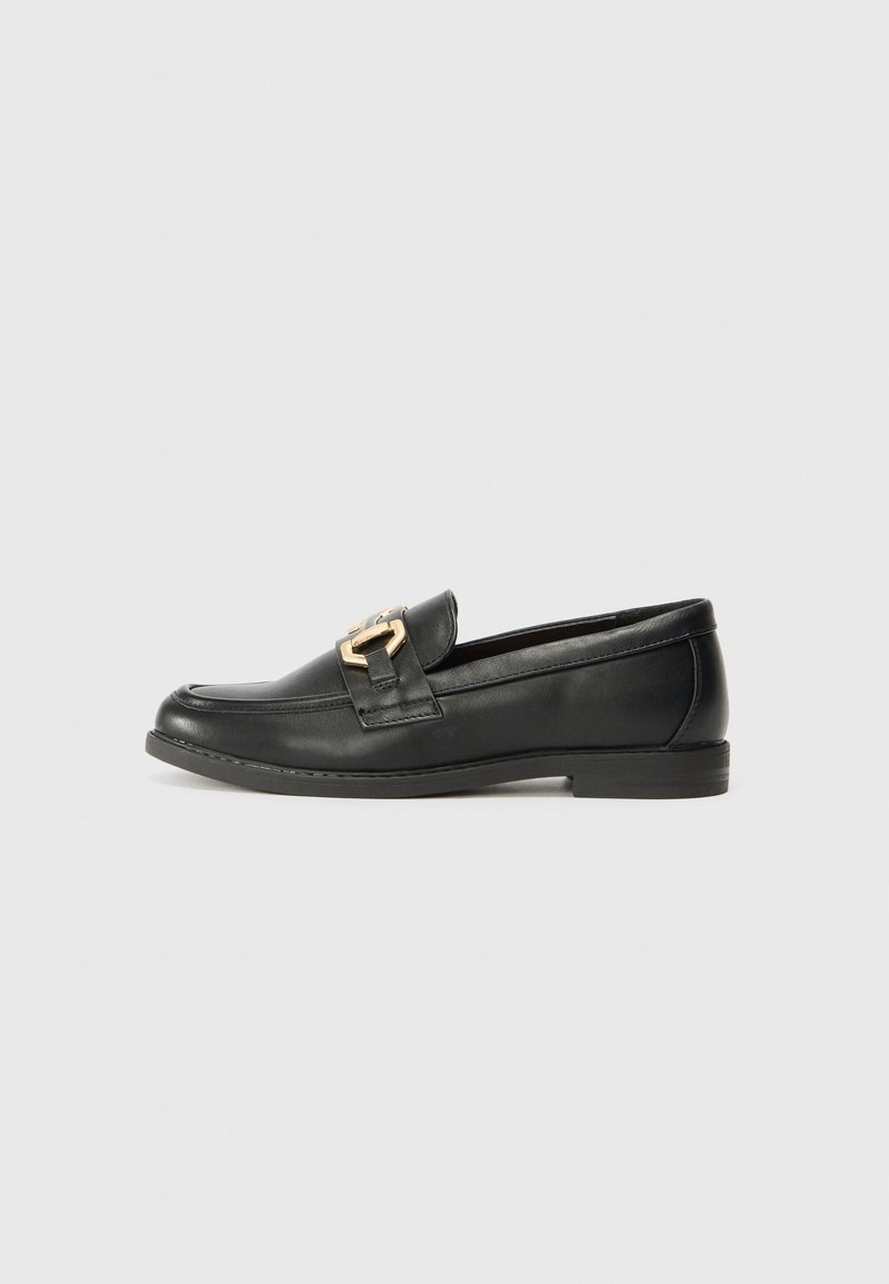 Mocassin en cuir noir avec petit talon et boucle en métal doré sur le dessus, présenté de profil gauche sur fond gris clair.