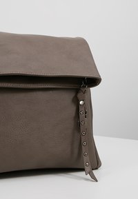 Borsa in pelle grigia con patta pieghevole, dotata di hardware argentato e una tracolla decorativa con borchie metalliche lungo il lato.