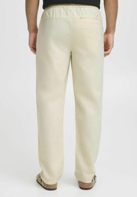 Beige brede bukser med elastisk taljebånd, der har en glat overflade og et enkelt design. Båret med lyse sandaler.