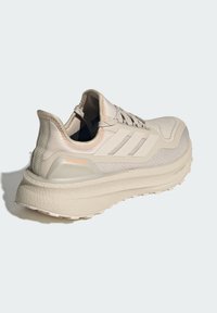 Béžová športová obuv s textúrovaným horným dielom z textilu, polstrovaným golierom a hrubou, odpruženou podrážkou. Má tri pruhy a nápis „ULTRABOOST“.