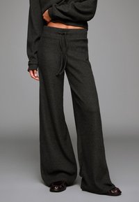 Donkergrijze wijde broek gemaakt van textiel met structuur, voorzien van een trekkoord in de taille en een lichte flair aan de onderkant. Flared silhouet, relaxte fit.