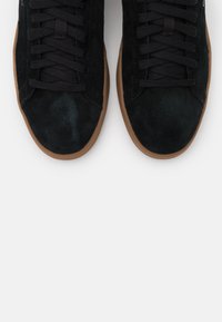 Sorte semskede sneakers med snøring foran, med sål af gummi. Teksturen er glat med en mat finish.