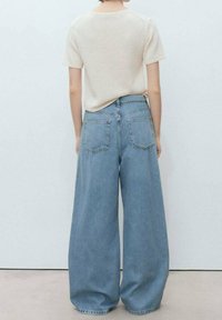 Helles beige kurzes Strickoberteil, kombiniert mit hoch taillierten, weit geschnittenen blauen Jeans aus Denim, die über Taschen auf der Rückseite und einen lässigen Schnitt verfügen.