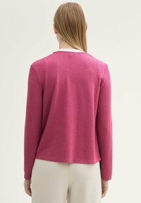 Fuchsia tröja med långa ärmar, texturerad tyg, och rund halsringning, med avslappnad passform och en något böjd fåll.