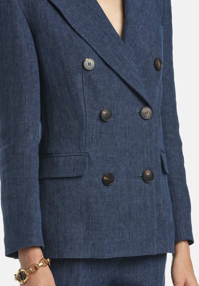 Navy blue double-breasted blazer with large black buttons, featuring a textured fabric and notched lapels. Side pockets included.