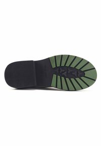 Suola di scarpa nera con accenti in gomma verde. Presenta scanalature orizzontali e una superficie testurizzata per una migliore aderenza. Il nome del marchio "NINE WEST" è visibile.