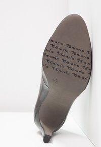 Semelle d'une chaussure à talon noir montrant la marque "Tamaris" et la taille 37 sur un fond clair.