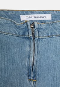 Světlé modré džínové kalhoty s předním zipem s kováním YKK, oranžovým prošíváním a štítkem s nápisem "Calvin Klein Jeans".