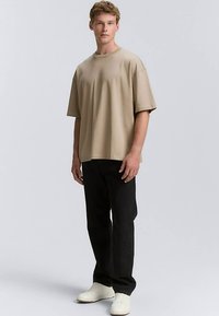 Bordinio atspalvio, laisvo silueto trumpomis rankovėmis marškinėliai iš minkštos medžiagos, derinami su juodomis tiesiomis kelnėmis ir baltais sportbačiais.