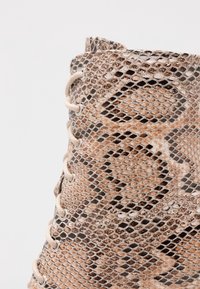 Snörade anklar stövlar gjorda av texturerat faux ormskinn i nyanser av brunt och beige, med silverögon och gräddfärgade snörningar.