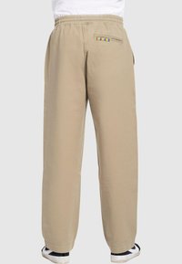 Beige Baumwollhose mit relaxed Fit, elastischem Bund und einer Gesäßtasche mit einem mehrfarbigen gestreiften Akzent.