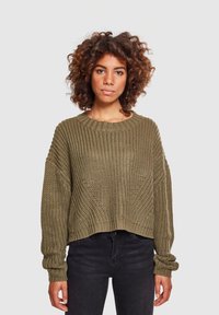 Pull en tricot épais de couleur vert olive avec un col rond, des épaules tombantes et des poignets côtelés. Longueur cropped avec un motif texturé sur l'ensemble.