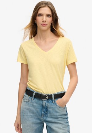 T-shirt jaune à col en V en tissu léger, à manches courtes, associé à un jean en denim bleu taille haute et une ceinture noire.