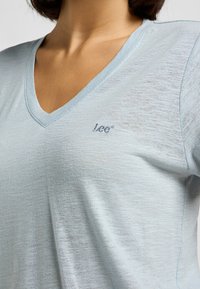 T-shirt azzurro chiaro a collo a V realizzato in tessuto morbido, con una leggera texture e il logo ricamato "Lee" sul lato sinistro.