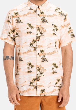 Korte mouwen overhemd met knopen, met een licht perzikkleurige achtergrond, print van palmbomen en eilanden, en oranje tekst, gedragen met een bruine broek.