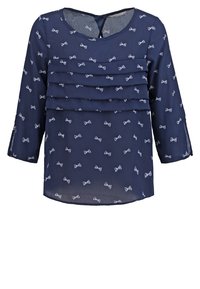 Blouse bleu marine en tissu léger, dotée de trois volants superposés, de motifs à nœuds et de manches longues avec des fentes décoratives.