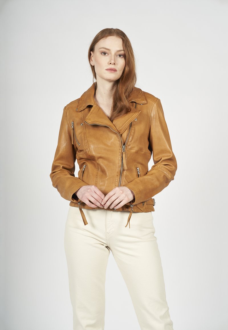 Skórzana motocyklowa kurtka w kolorze brązowym, o dopasowanym kroju, z asymetrycznym zapięciem na zamek i dwoma bocznymi suwakami. Posiada szerokie klapy i dekoracyjne akcesoria.