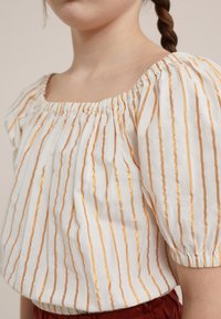Top bianco con strisce verticali dorate, scollo elasticizzato e maniche a palloncino, realizzato in tessuto leggero. Presenta una vita arricciata.