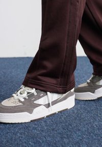 Šedé a biele tenisky z kvalitnej sieťoviny a semišu, so robustnou podrážkou a okrúhlou špičkou, skombinované s burgundskými nohavicami.