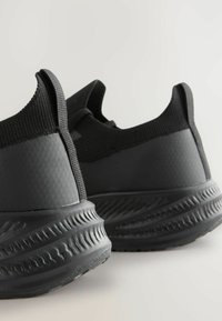 Chaussures de sport noires avec une tige texturée, un col en tissu élastique et une semelle rembourrée avec un motif en vagues.